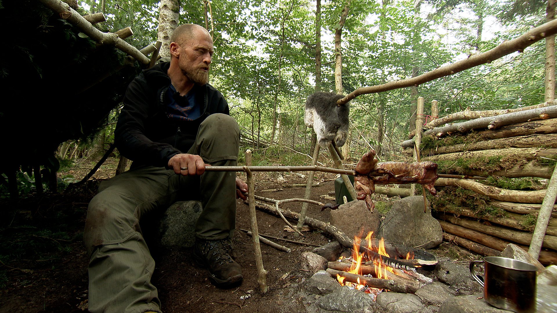 Deltager Klaus Rogild steger en kanin i sin hjemmebyggede lejr i en skov i Vesthimmerland.